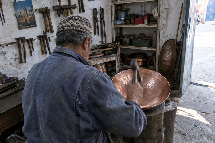 Artisan hammering a copper basin on an anvil in a Fes workshop