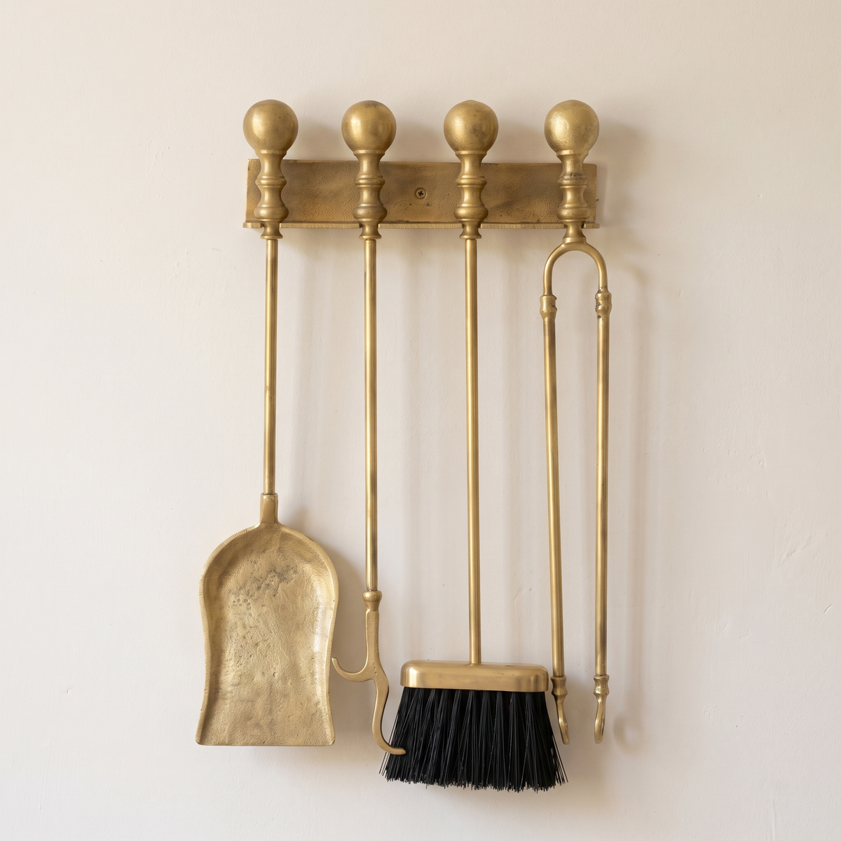 Brass wall rack with ball finials holding shovel, poker, brush and tongs on a light background
