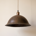 Aged copper bell pendant with flared rim and beige cord on a light background