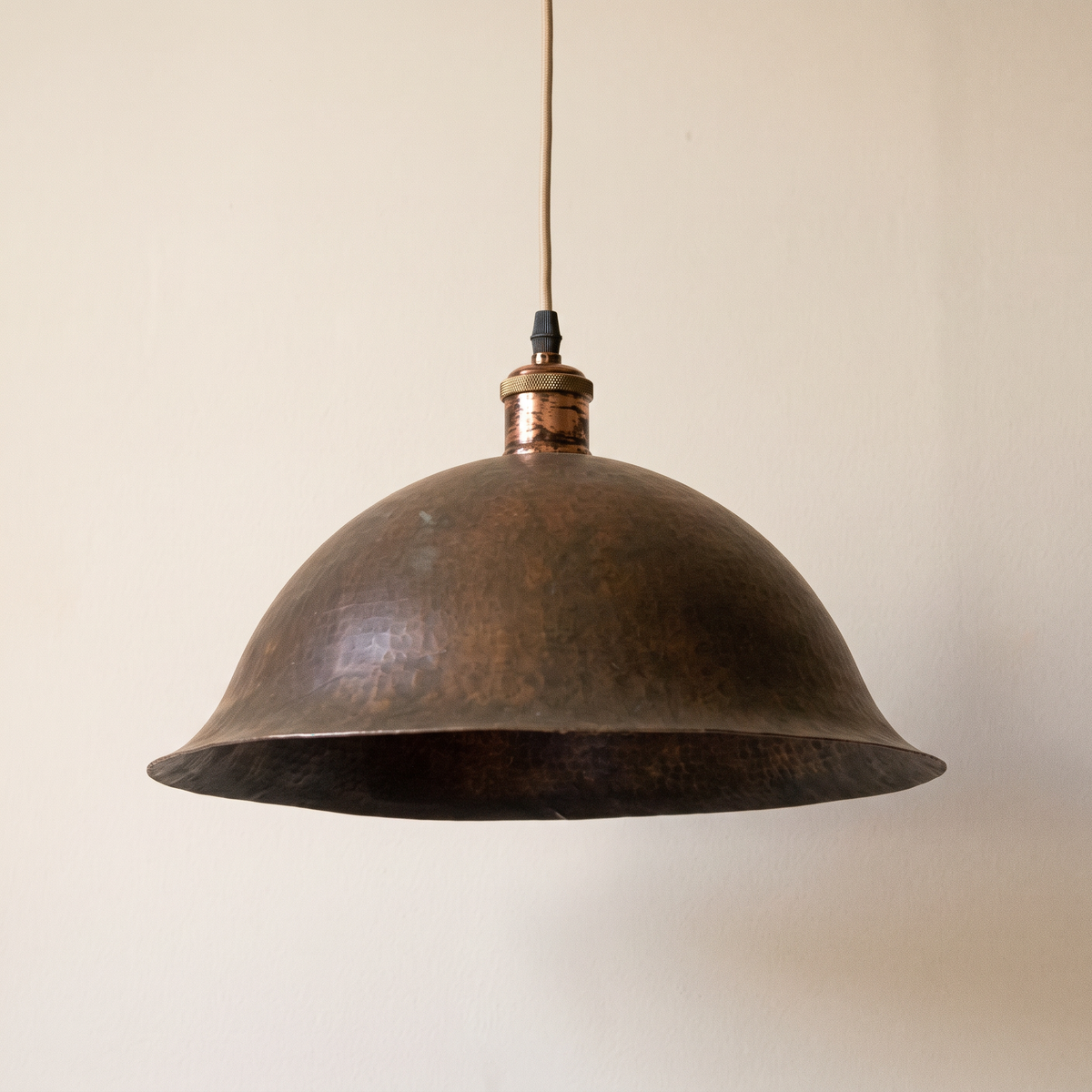 Aged copper bell pendant with flared rim and beige cord on a light background