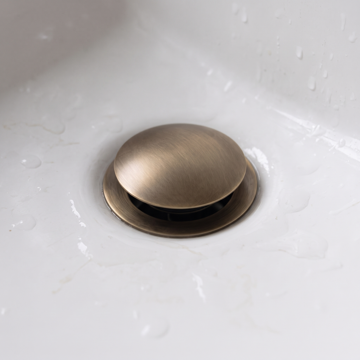 Close view of the aged brass domed drain cap in a white basin