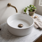 Antique brass pop-up drain in a white vessel basin on a marble vanity