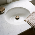 Antique brass drain cap in a white undermount basin with soap and linen