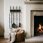 Dark black fireplace tools hung beside a limestone fireplace with a log basket