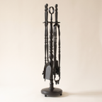 Black fireplace tool set with ring-top stand, shovel, poker, tongs and brush on a light background