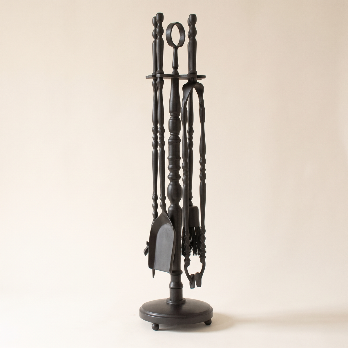 Black fireplace tool set with ring-top stand, shovel, poker, tongs and brush on a light background
