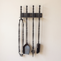 Black wall rack with tongs, shovel, leaf-tip poker and brush on a light background