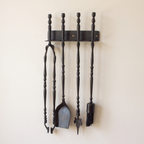 Black wall rack with tongs, shovel, leaf-tip poker and brush on a light background