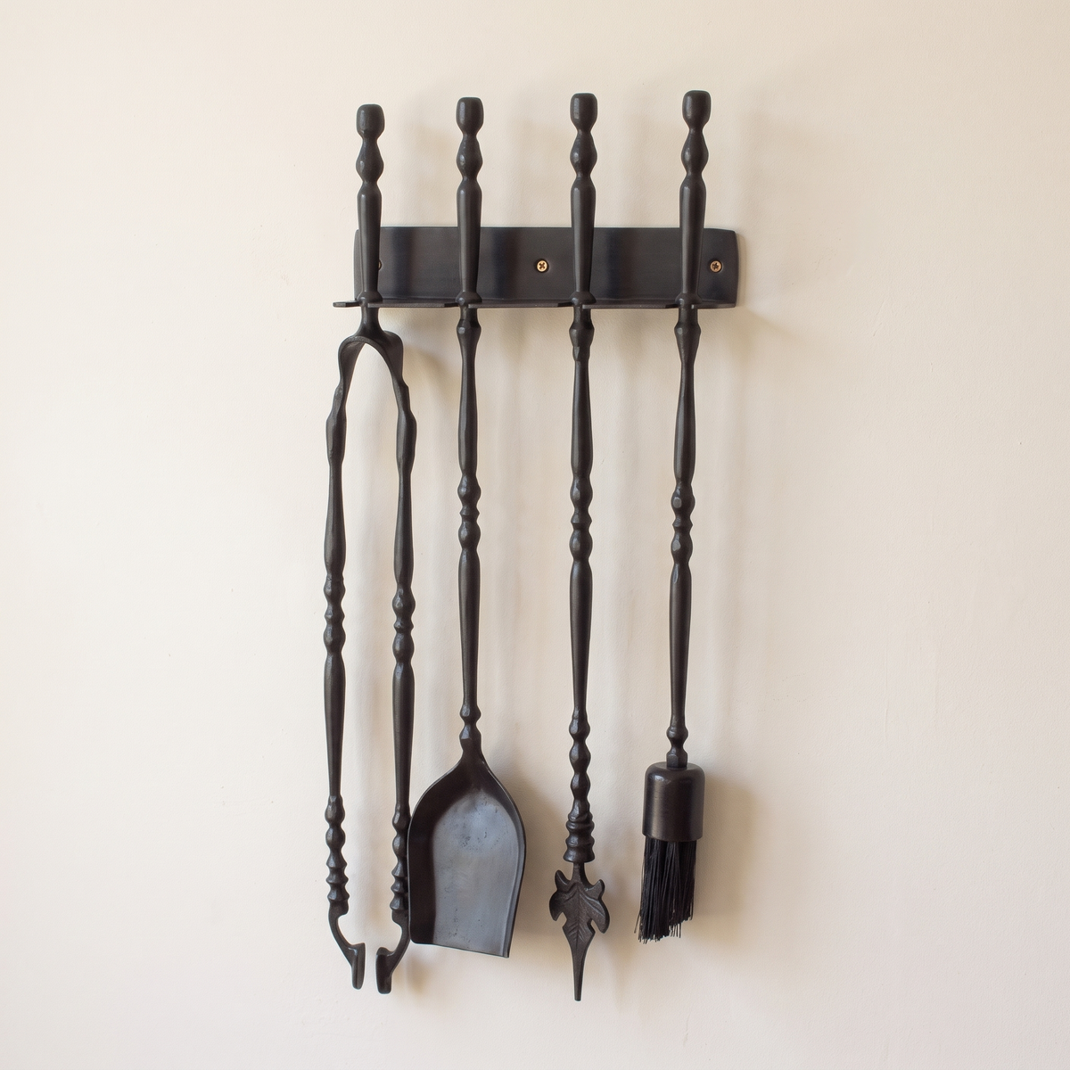 Black wall rack with tongs, shovel, leaf-tip poker and brush on a light background