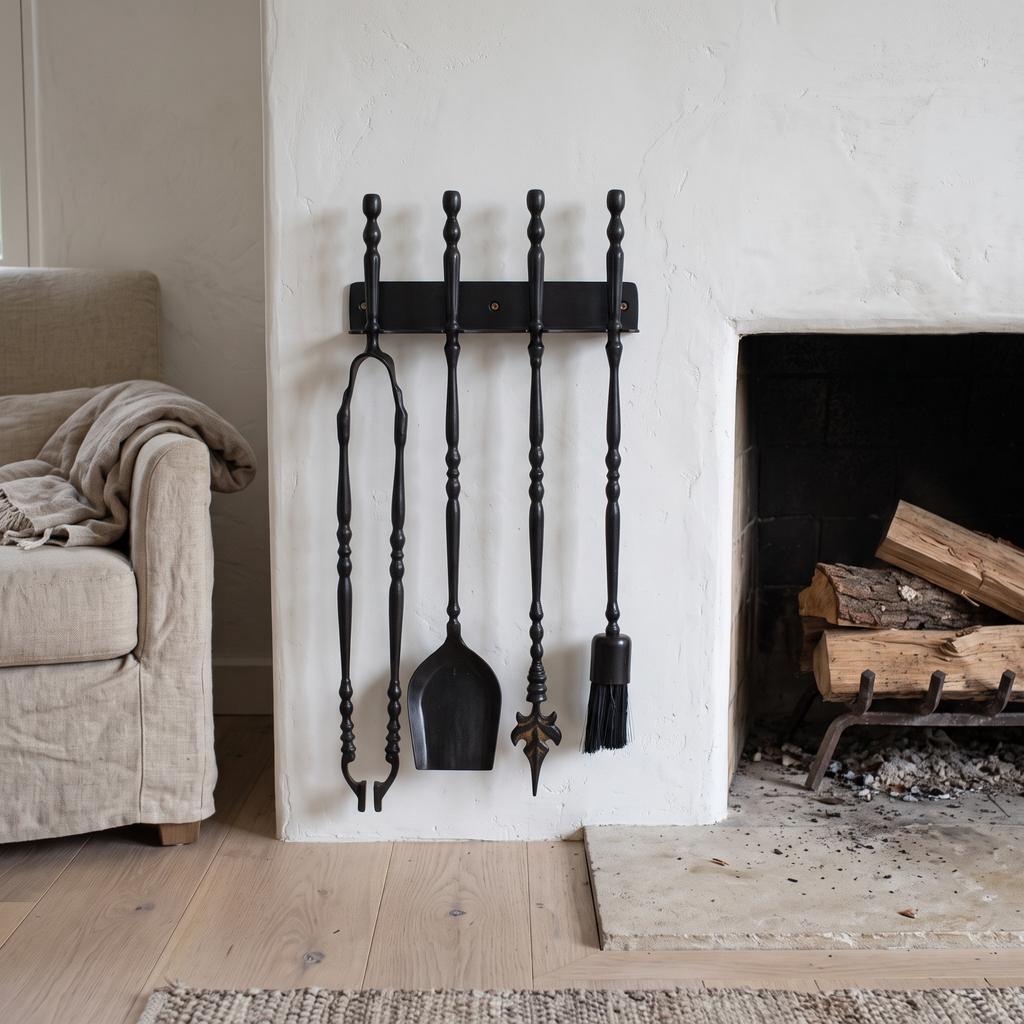 Black brass fireplace tools on a wall rack beside a white plaster fireplace