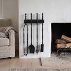 Black brass fireplace tools on a wall rack beside a white plaster fireplace
