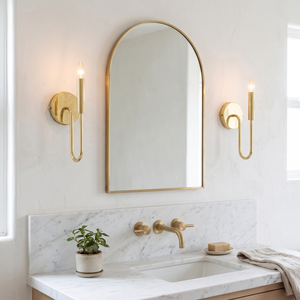 Pair of brass curved arm candle sconces either side of an arched bathroom mirror