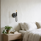 Oil rubbed bronze curved arm candle sconce beside a bed