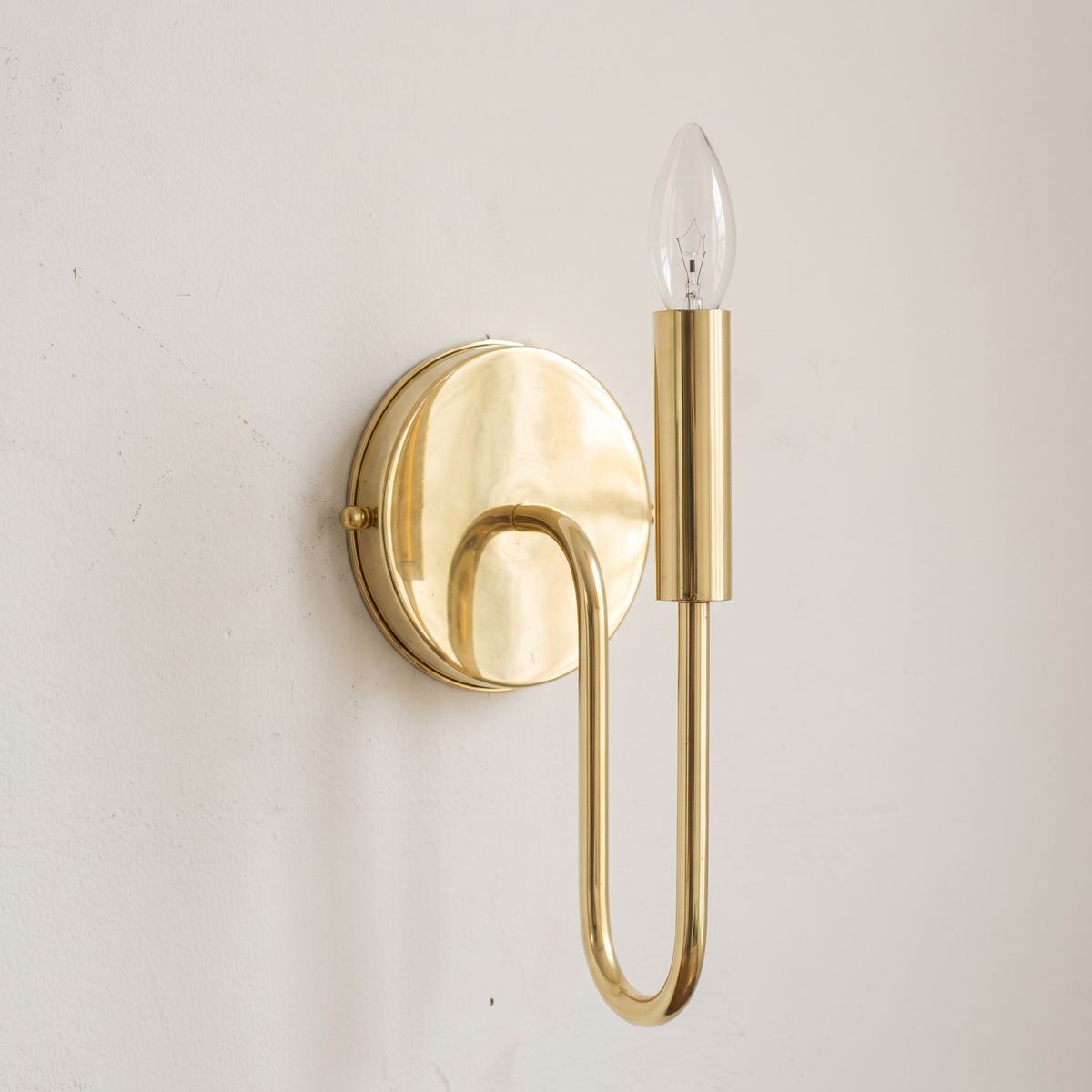 Unlacquered brass curved arm candle wall sconce on a light background