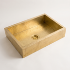 Solid brass apron-front farmhouse sink with hammered basin and brass basket strainer