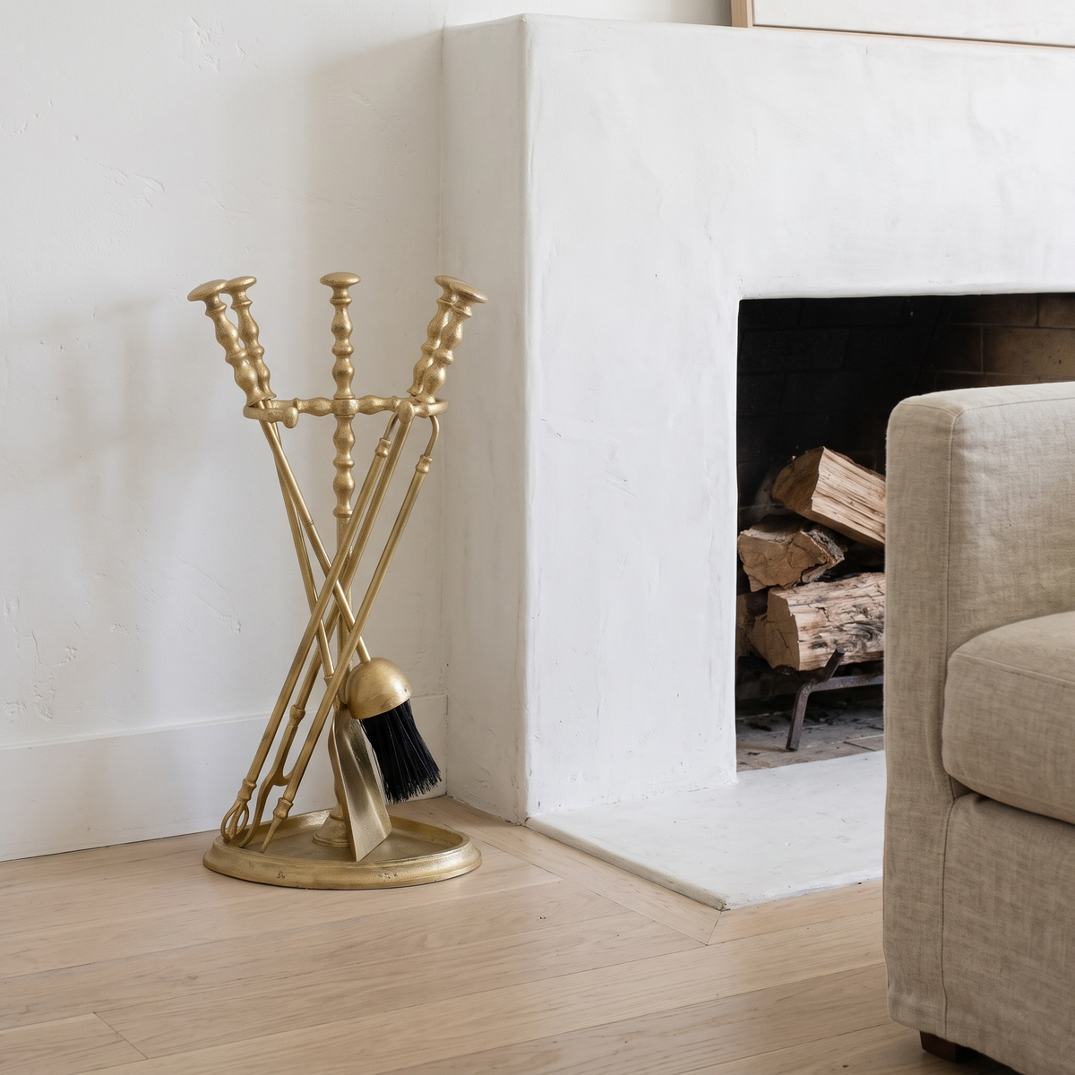 Satin brass fireplace tools on a half-round stand beside a white plaster fireplace