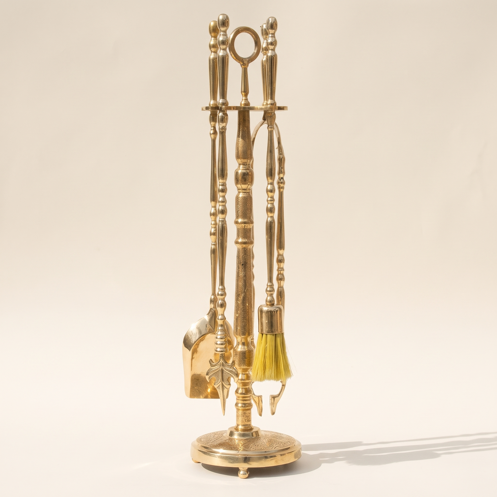 Brass fireplace tool set with shovel, brush, poker and tongs on a turned stand, light background