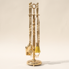 Brass fireplace tool set with shovel, brush, poker and tongs on a turned stand, light background