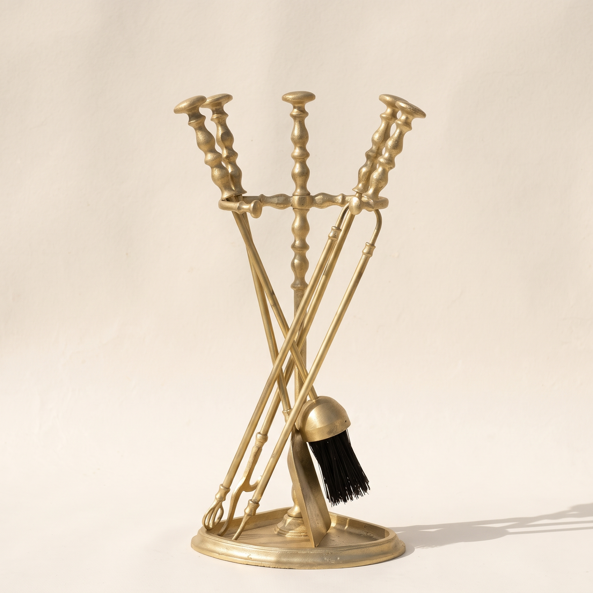 Brass fireplace tool set with tongs, poker, shovel and brush on a half-round base, light background
