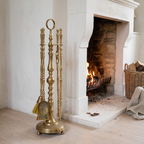 Brass fireplace tool set standing beside a limestone fireplace with a log basket