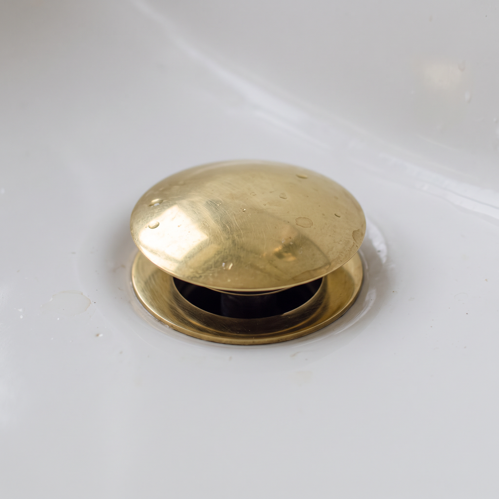 Close-up of the domed brass push-up drain cap raised open in a white basin
