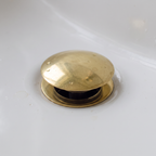 Close-up of the domed brass push-up drain cap raised open in a white basin