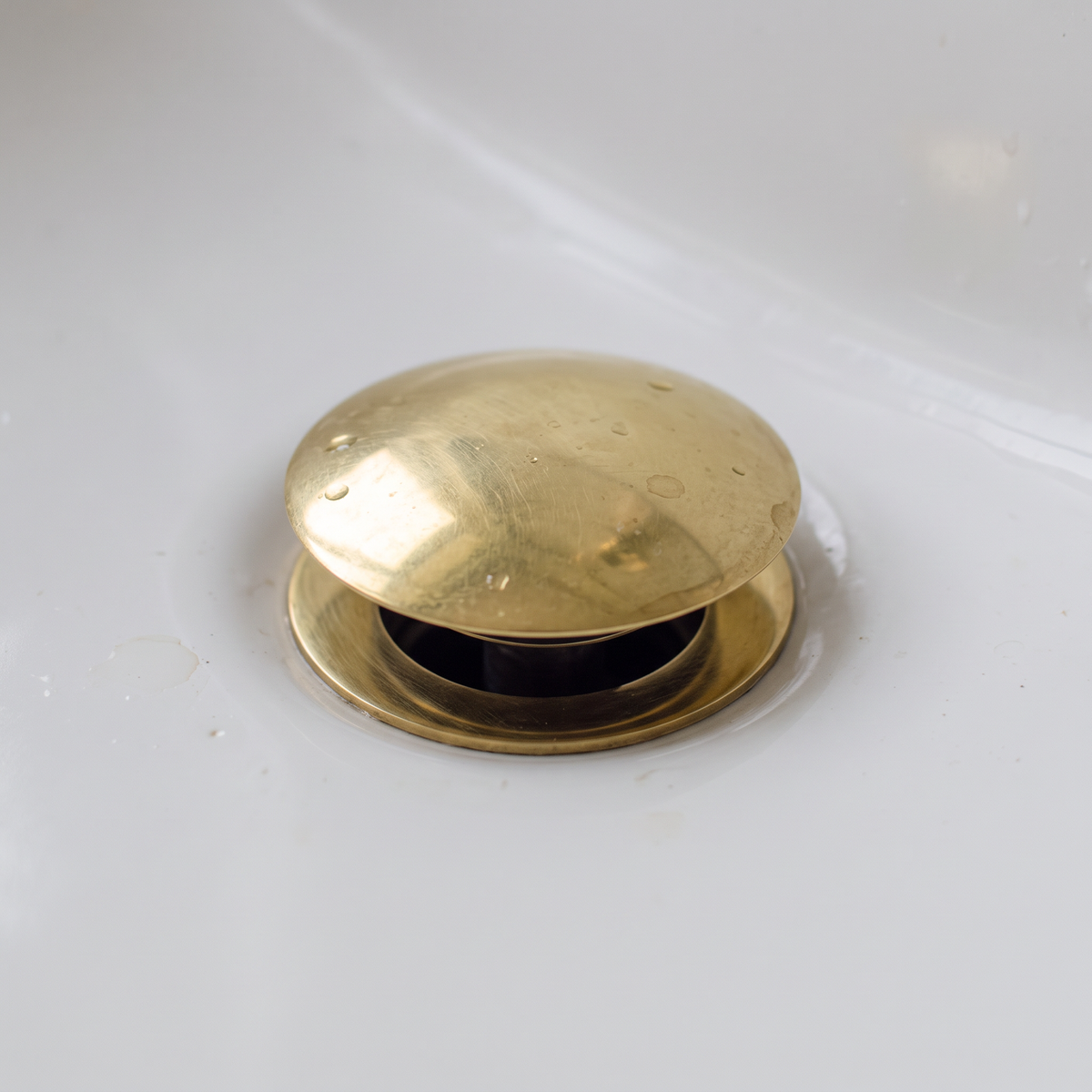 Close-up of the domed brass push-up drain cap raised open in a white basin