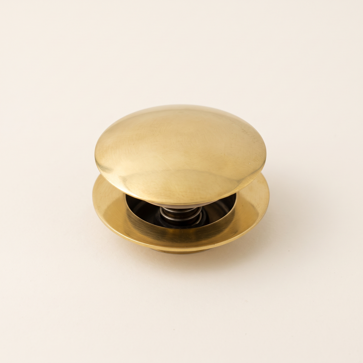 Brass push-up drain with domed cap and flange on a light background