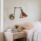 Brass swing arm sconce with copper shade used as a reading light beside a bed
