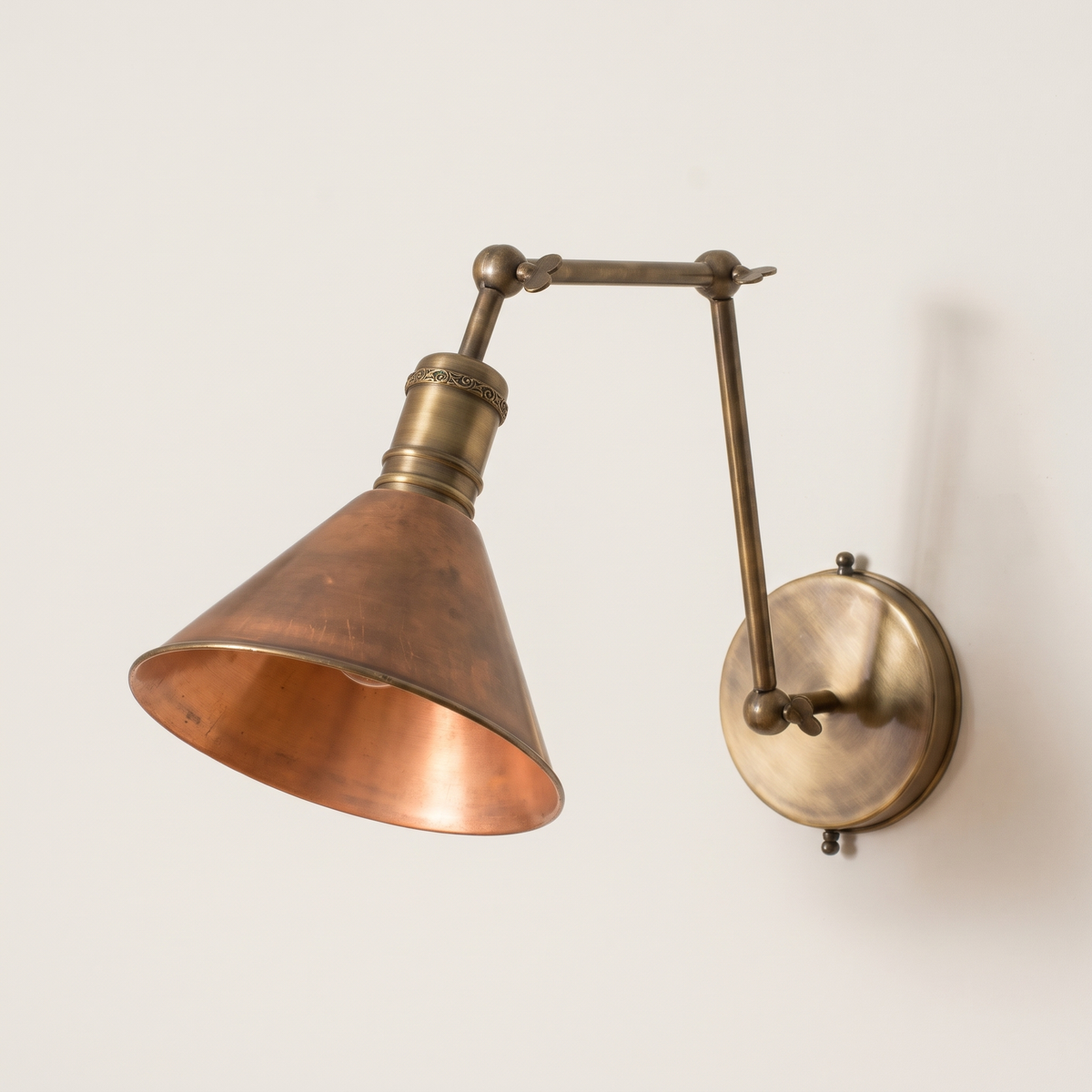 Aged brass swing arm wall sconce with copper cone shade on a light background