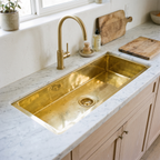 Brass undermount prep sink with brass basket strainer in a bright white oak kitchen