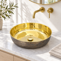 Bronze and brass round vessel sink on a sunlit white marble bathroom vanity