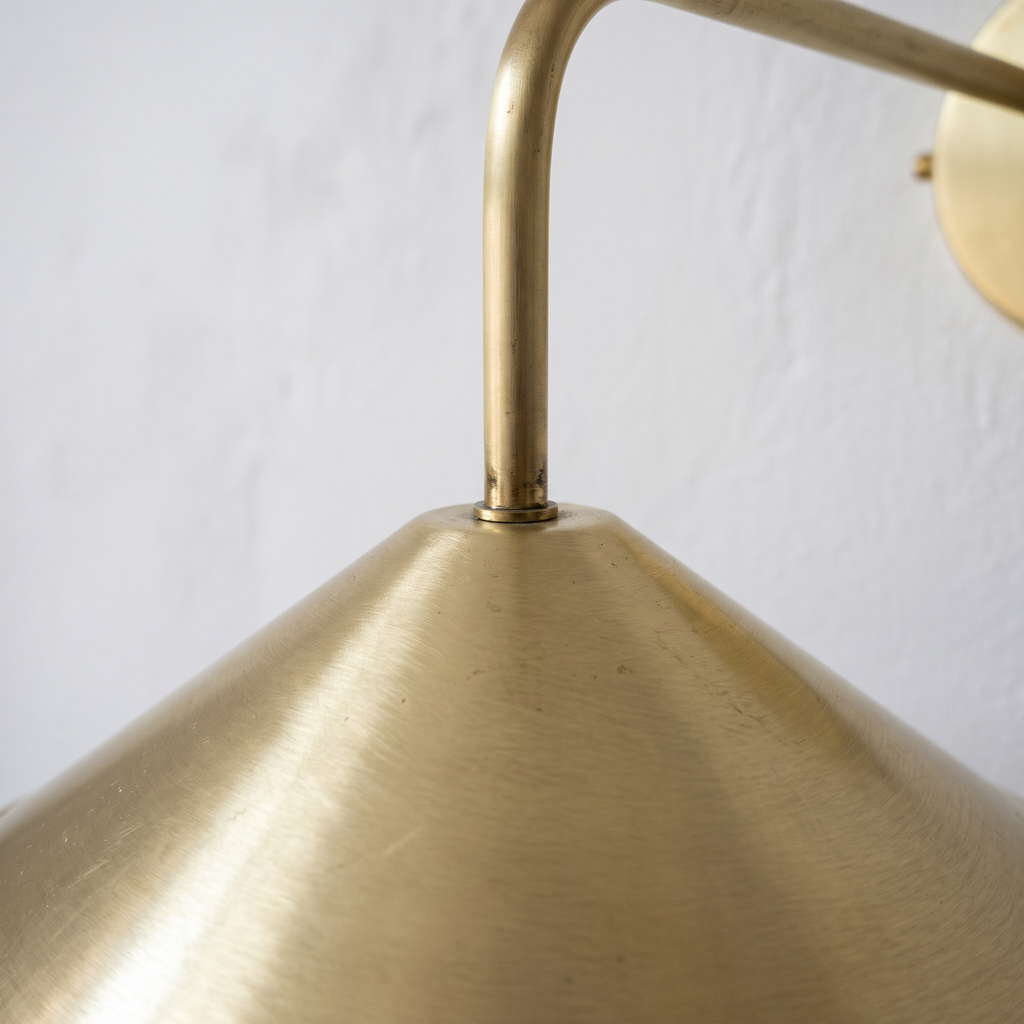 Close-up of the brushed brass cone shade where the slim arm meets the pointed top