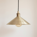 Brushed brass cone pendant light with knurled brass socket and black cord on a light background
