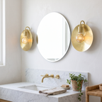 Pair of brushed brass dish wall sconces either side of a round bathroom mirror