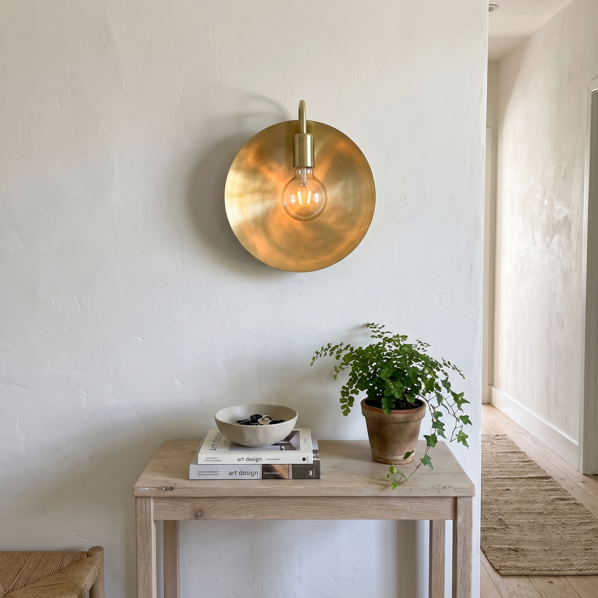 Brushed brass dish wall sconce above a white oak hallway console