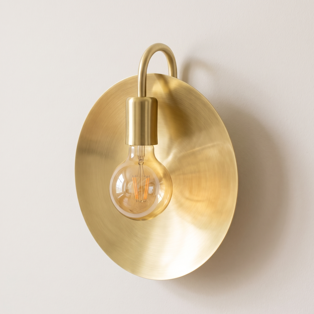 Brushed brass dish wall sconce with round disc and globe bulb on a light background