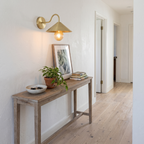 Brushed brass gooseneck cone shade wall sconce above a white oak hallway console