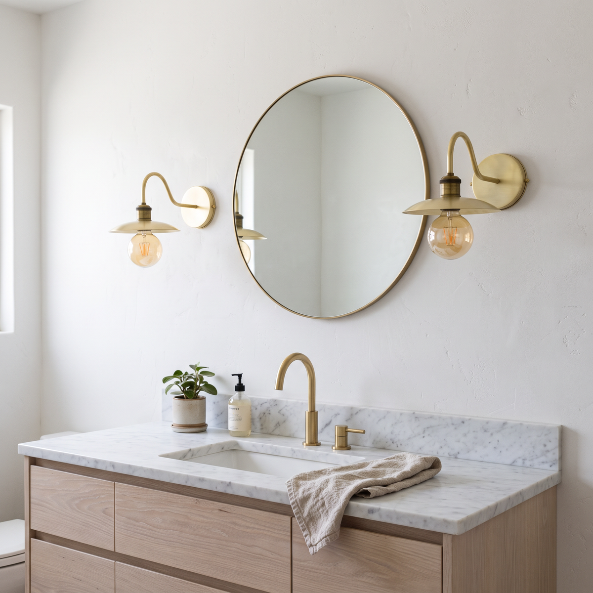 Pair of brushed brass gooseneck wall sconces beside a round bathroom mirror