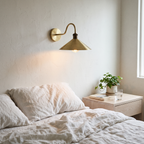 Brushed brass swan neck cone shade sconce beside a bed with linen bedding