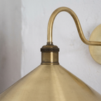 Close-up of the curved brass arm, knurled antique brass socket and brushed cone shade