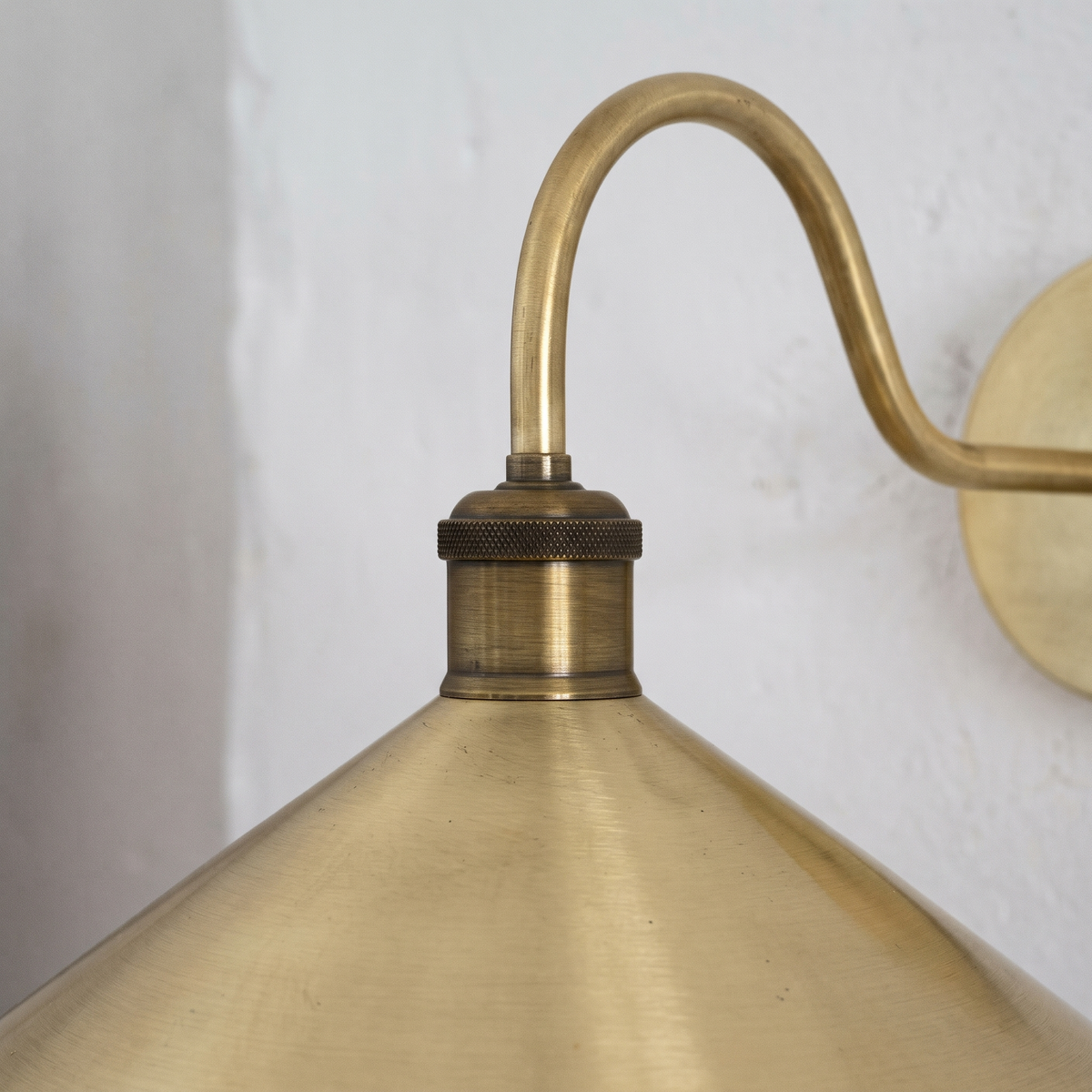 Close-up of the curved brass arm, knurled antique brass socket and brushed cone shade
