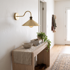 Brushed brass swan neck cone shade sconce above a white oak hallway console
