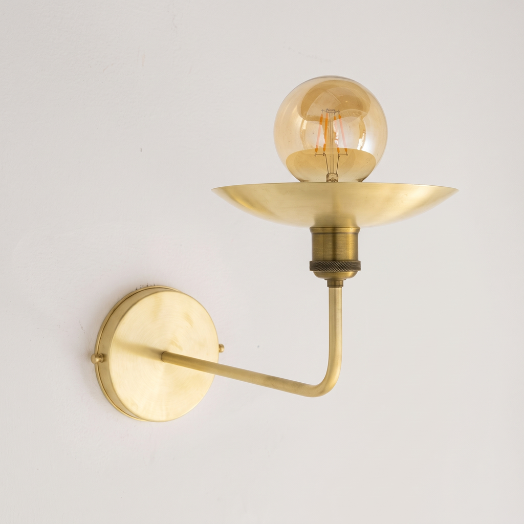 Brushed brass uplight wall sconce with saucer dish and globe bulb on a light background