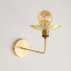 Brushed brass uplight wall sconce with saucer dish and globe bulb on a light background