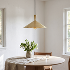 Brushed brass wide cone pendant over a round white oak dining table