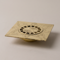 Engraved brass square floor drain with floral pattern on a light background