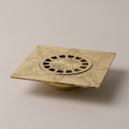 Engraved brass square floor drain with floral pattern on a light background