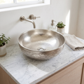 Engraved round German silver vessel sink on a white marble vanity with a wall-mounted nickel spout