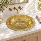 Engraved oval brass drop-in sink in a sunlit white marble bathroom vanity